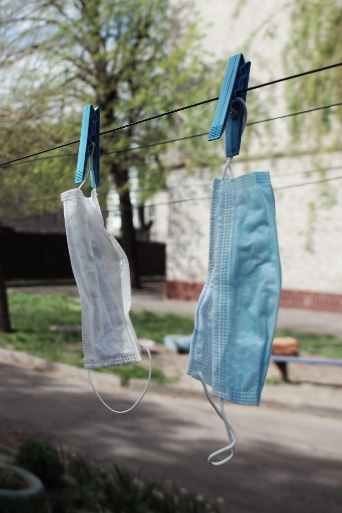 7. A photograph of two medical masks hanging to dry on a clothesline. The mask on the left is white and the mask on the right is blue. Each is pinned to the line with a light blue clothespin.