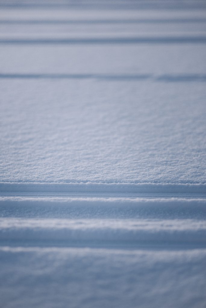 A close-up photograph of smooth, freshly fallen snow on a flat street.
