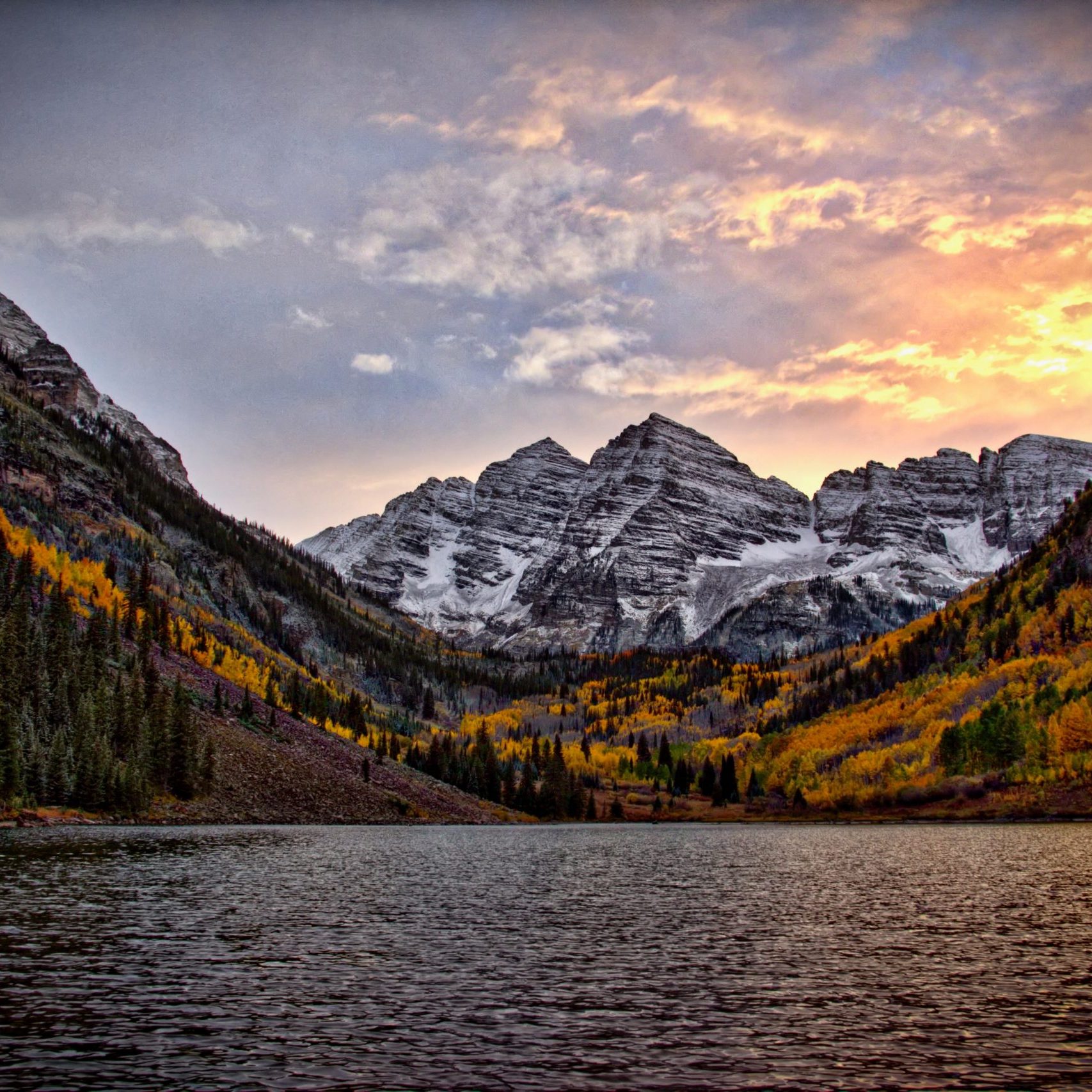 Coucher de soleil sur un lac et des bois d'automne au pied d'une montagne